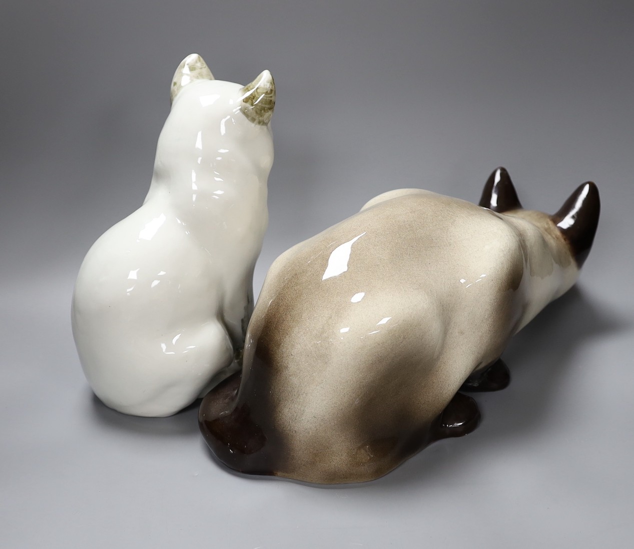 A Kensington ceramic lurking Siamese cat with blue glass eyes by Winstanley, together with another, tallest 26cm